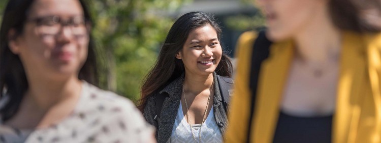 Hero image of a young female student walking with 2 people in front of her blurred out