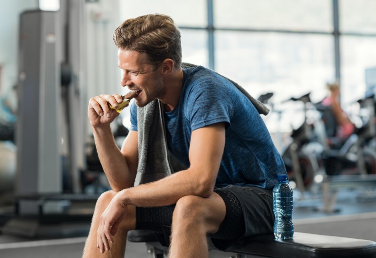 Male eating an energy bar inside a gym.