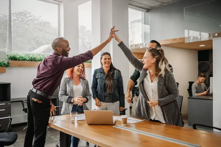 Diverse business team celebrating and giving high fives during boardroom meeting