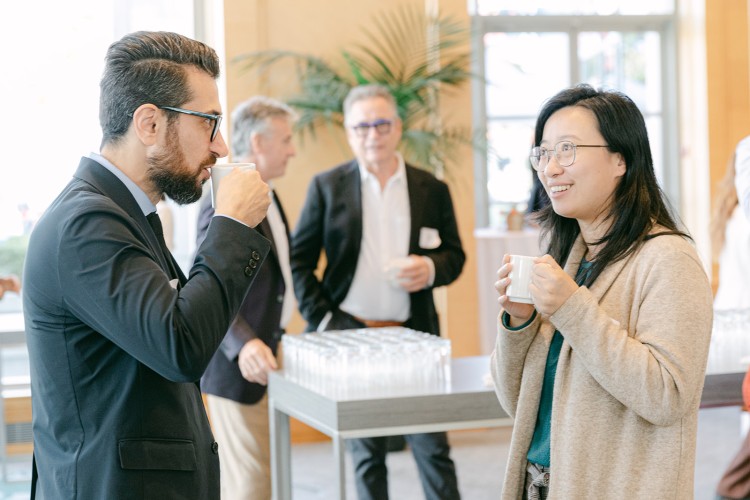 A group of people sipping coffee and chatting at an alumni breakfast eventin a hotel