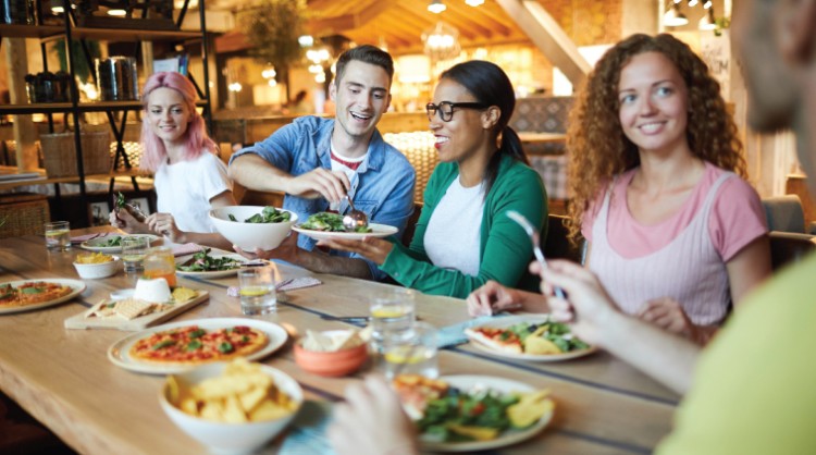 A mixed group of men and women at a table eating, smiling and socialising 